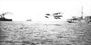 The first seaplane carrier, the French La Foudre (right, with hangar and crane), with one of her Canard Voisin seaplanes taking off, during tactical exercises in June 1912.